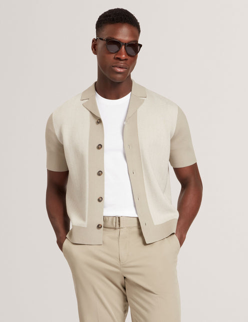 A male model wearing a short sleeve knitted shirt in beige color with a revere collar and button-through design, paired with light beige trousers and sunglasses.